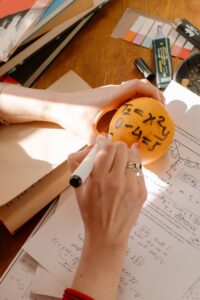 Person sitting at desk studying, has previous question papers in front of them, writing formulas on an orange
