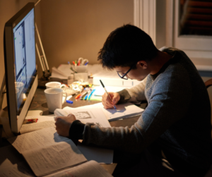 A learner on a desk studying on his books and a computer screen